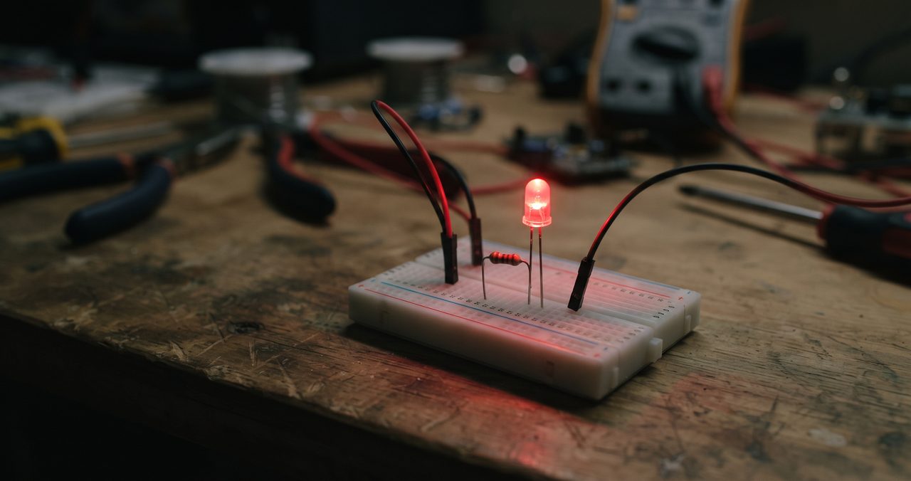 暗めの室内でブレッドボードに配線された赤色LEDが点灯している様子、電子工作の実践をイメージさせる情景