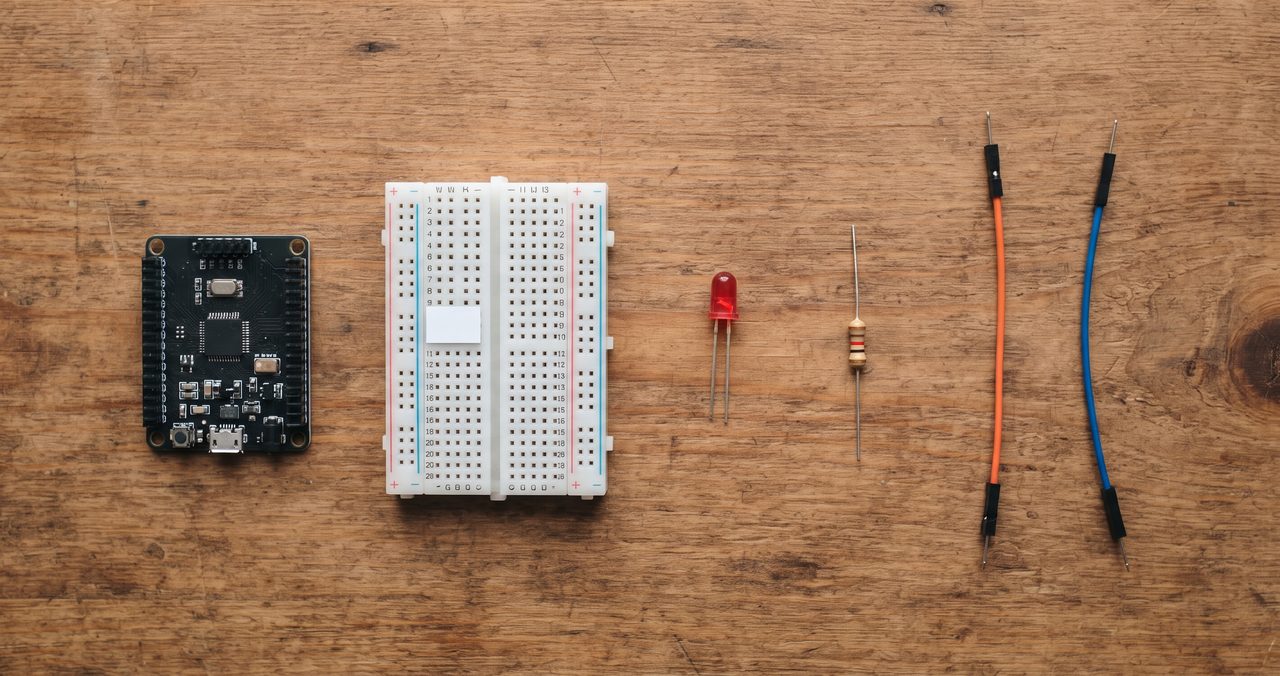 マイコンボード、ブレッドボード、LED、抵抗器、ジャンパー線2本の5点の部品が机の上に俯瞰で並べられている物撮り写真