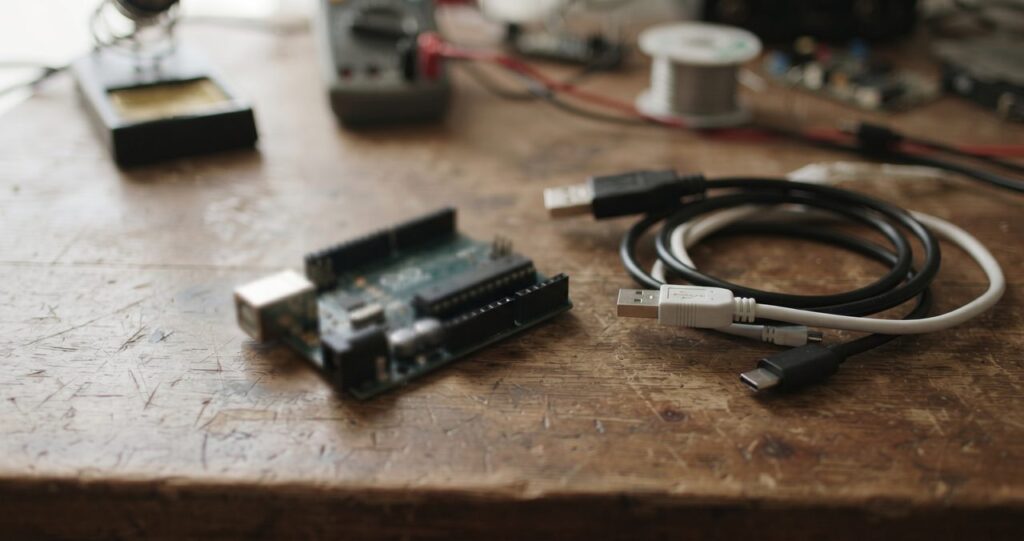 机の上に置かれたマイコンボードと少し絡まった状態のUSBケーブル、トラブルシューティングを連想させるやや雑然とした情景