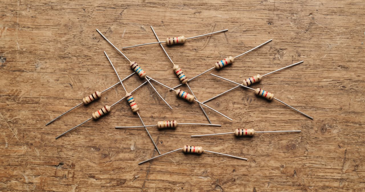 小さな円筒形の抵抗器が10本前後、木製の机の上に散らばって置かれている様子を俯瞰で撮影した物撮り写真